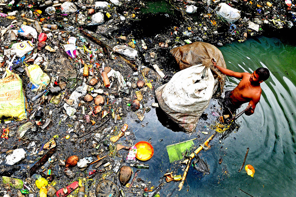 Un recogedor de basura se sumerge hasta la cintura en el agua de un canal de Kochi (India).